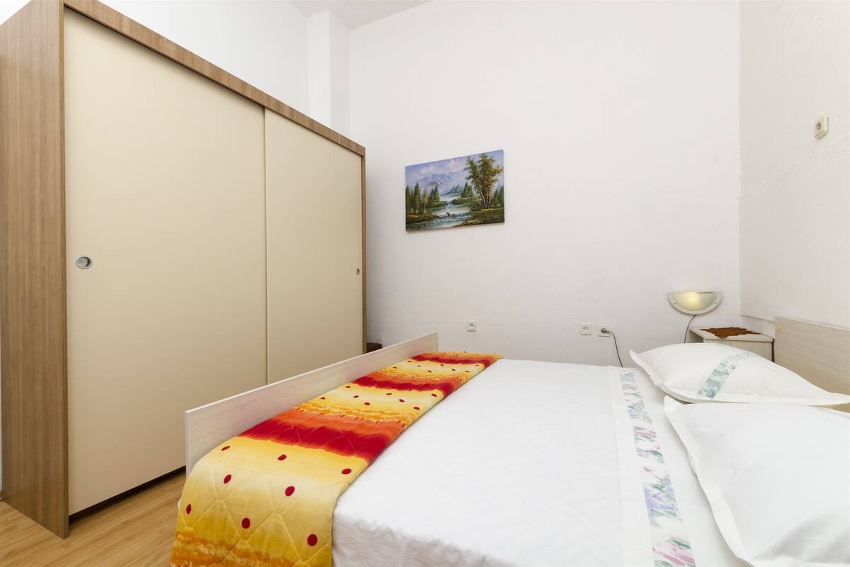 A bedroom with a bed, a wardrobe, a painting, and a bedside table.