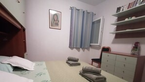 Un dormitorio con cama, una silla, cómoda, espejo y estante con libros.