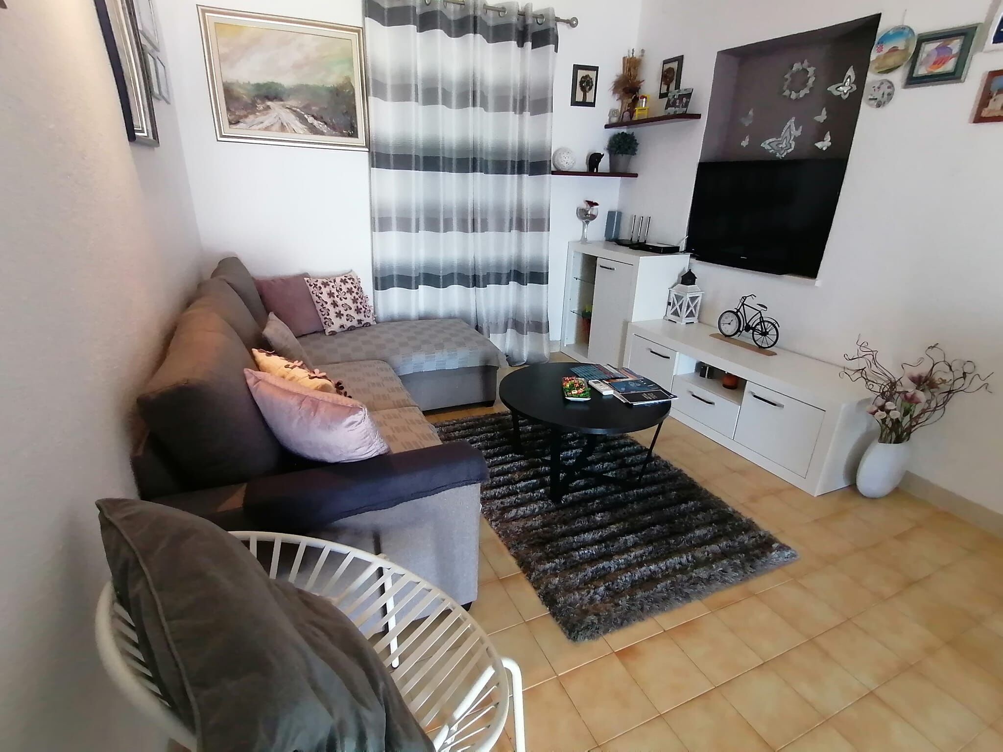 A living room with a sofa, a coffee table, a TV, and a small white chair.