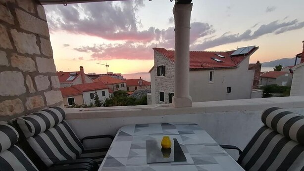 Una terraza con una mesa y cojines a rayas, con vistas a un pueblo de tejados rojos y un atardecer.
