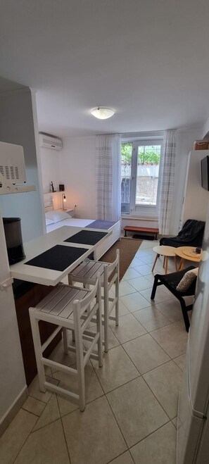 Habitación de hotel compacta con kitchenette, cama, mesa de comedor con sillas y un pequeño rincón de estar con mesa y sillas.