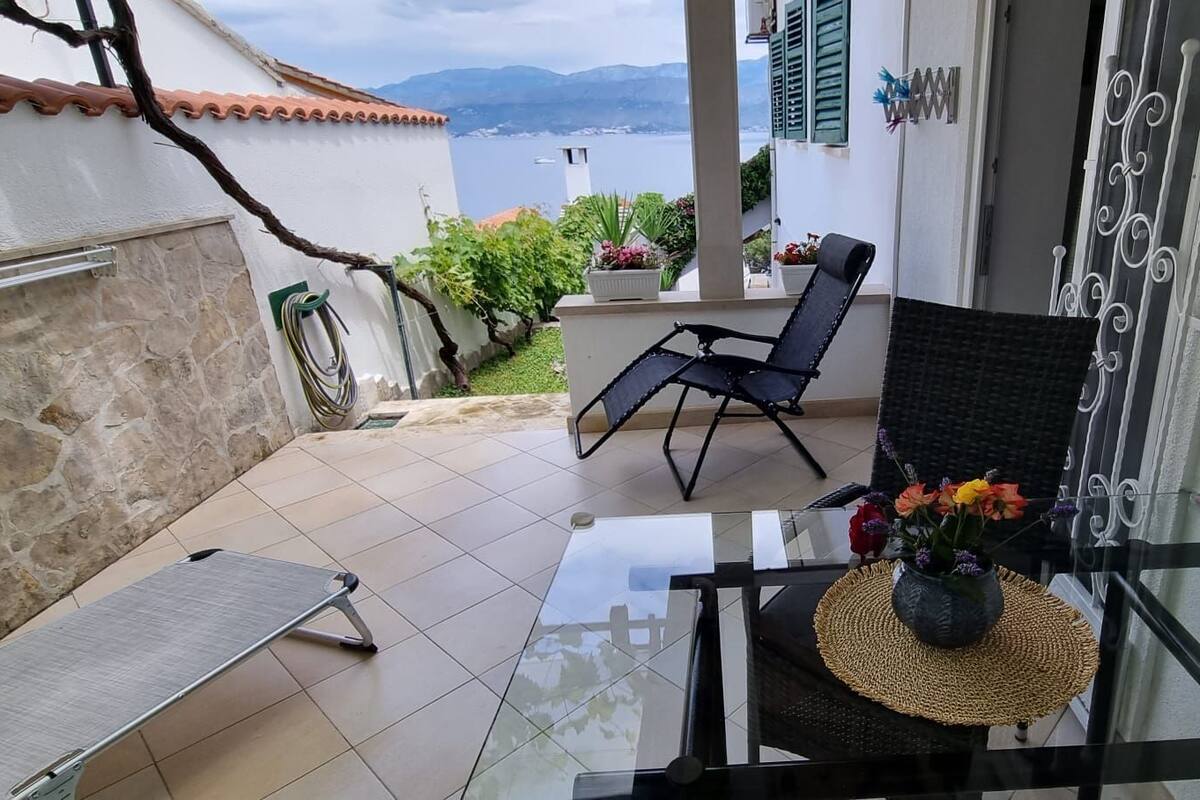 A balcony with a glass table, two black chairs, a wicker chair, and a bench.