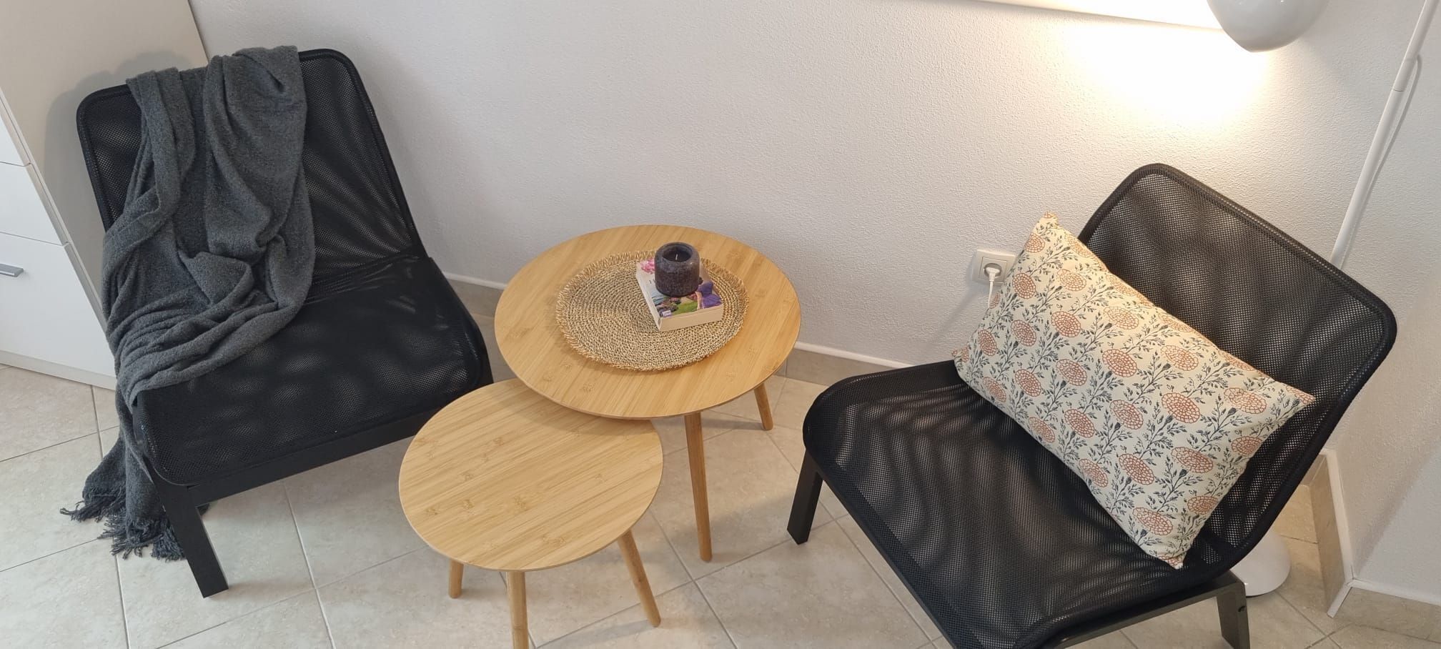 A room with a black chair, a small round wooden table, and a lamp.