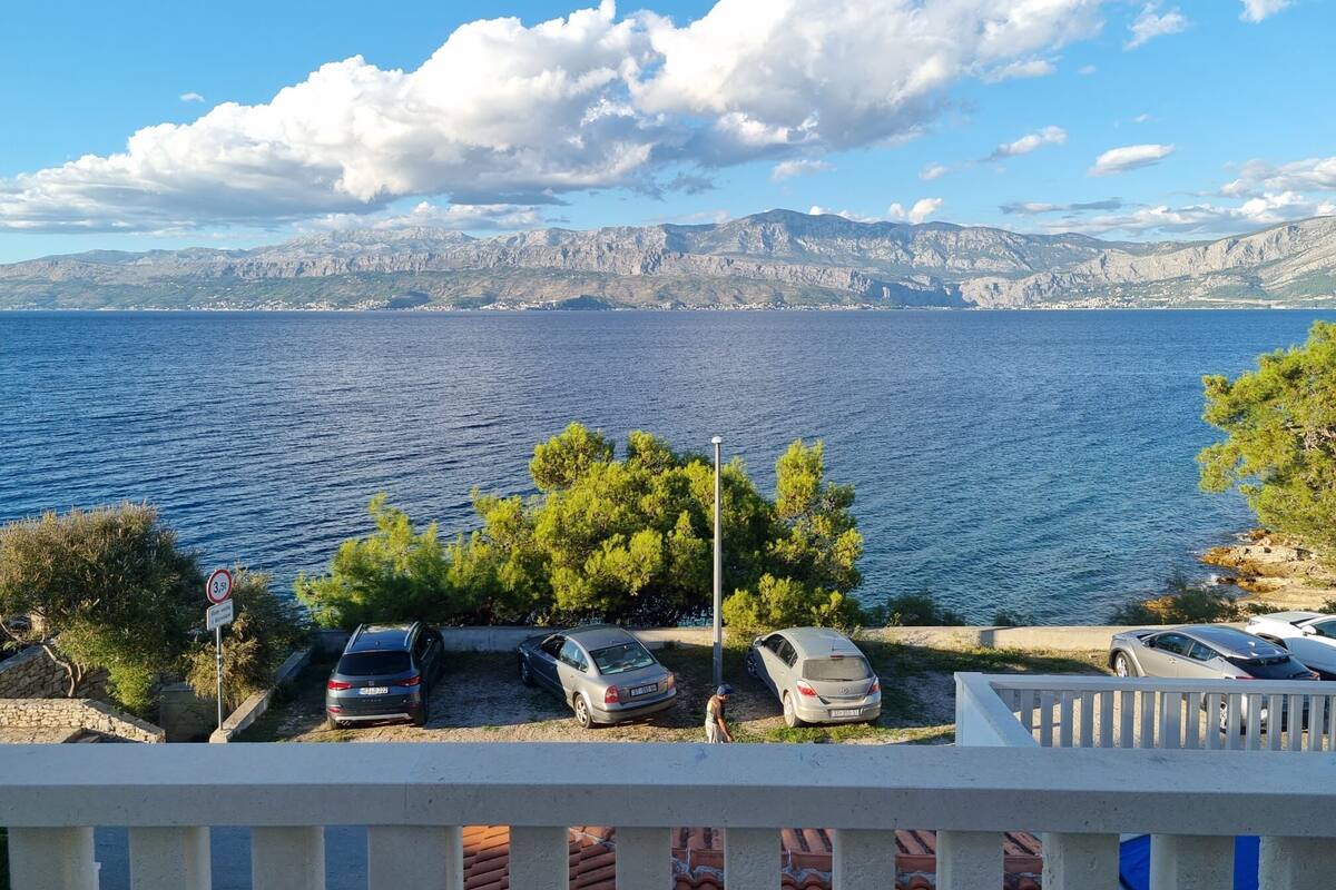 A coastal view with parked cars, a clear sky, and distant mountains.