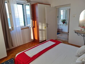 Un dormitorio con cama, armario, ventana con cortinas y vistas al exterior.