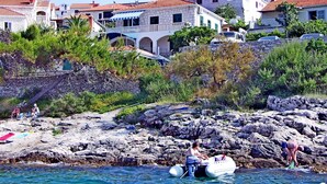 A coastal area with stone buildings, rocky shoreline, and a small boat with people. - Apartments Hani (Postira)
