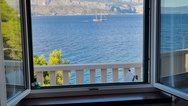 A room with a view of a sea and mountains, a table with a bowl, and a hanging light fixture. - Apartments Hani (Postira)