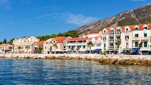 A coastal town with buildings along the waterfront, featuring balconies and a stone wall separating the buildings from the water. - Apartment Sunny Apartment (Bol)