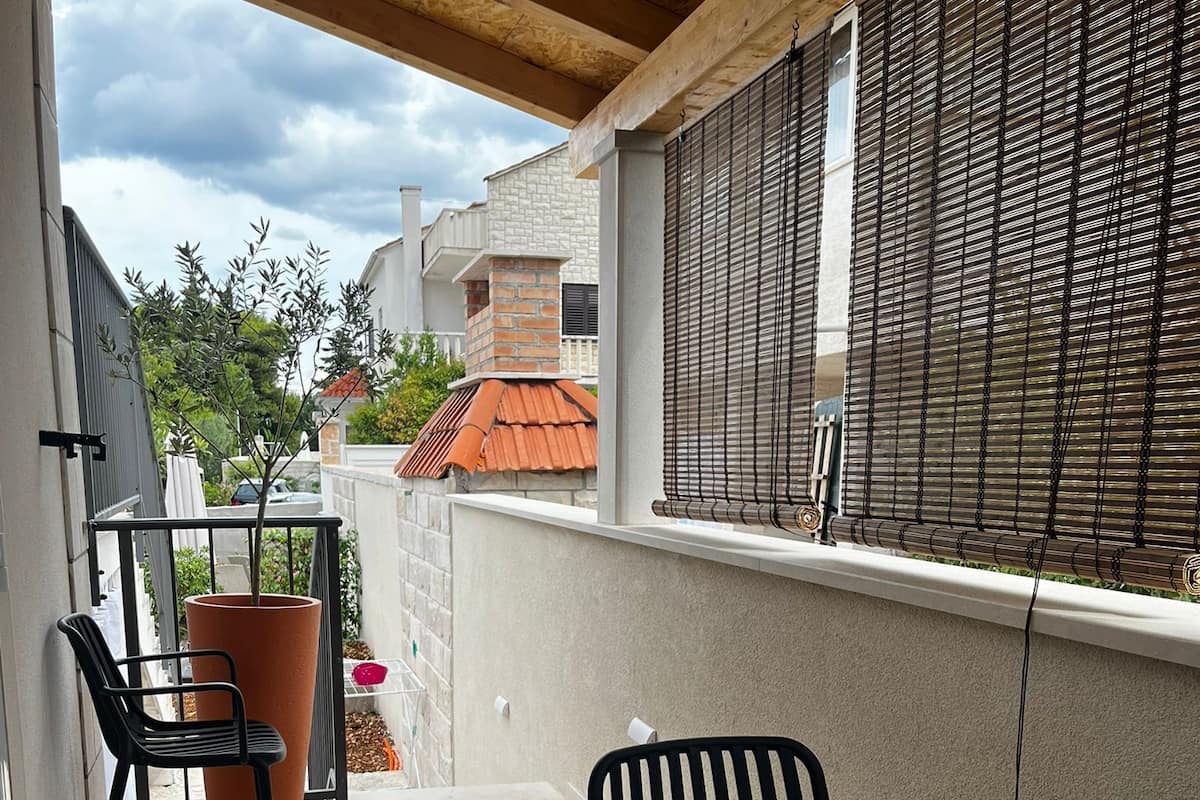 A covered patio with a table and chairs, a potted plant, and a view of neighboring buildings.