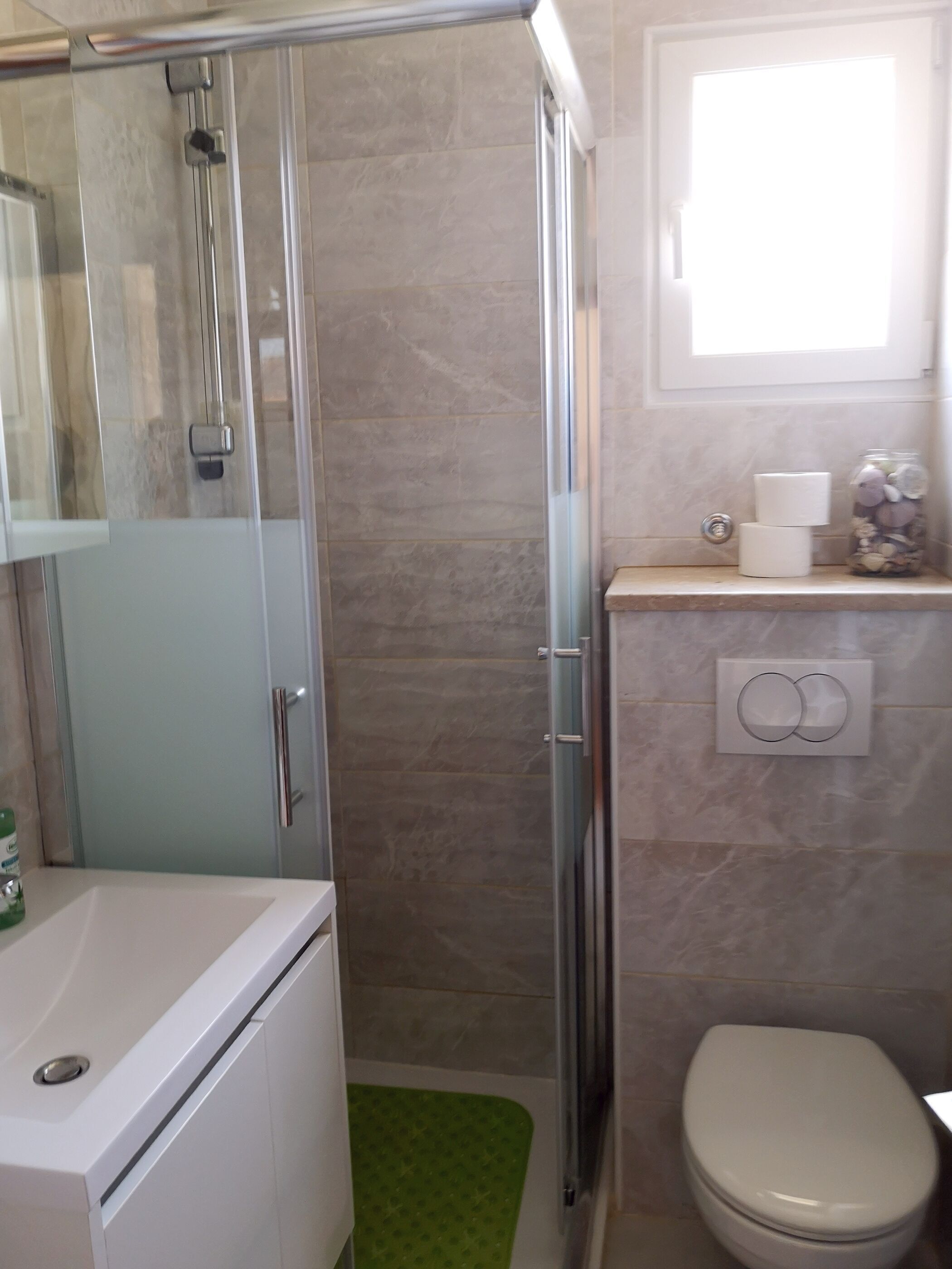 A bathroom with a glass shower enclosure, a toilet, and a sink.