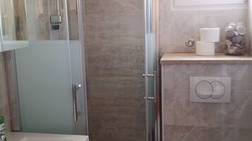 Un baño con cabina de ducha de vidrio, inodoro y lavamanos.