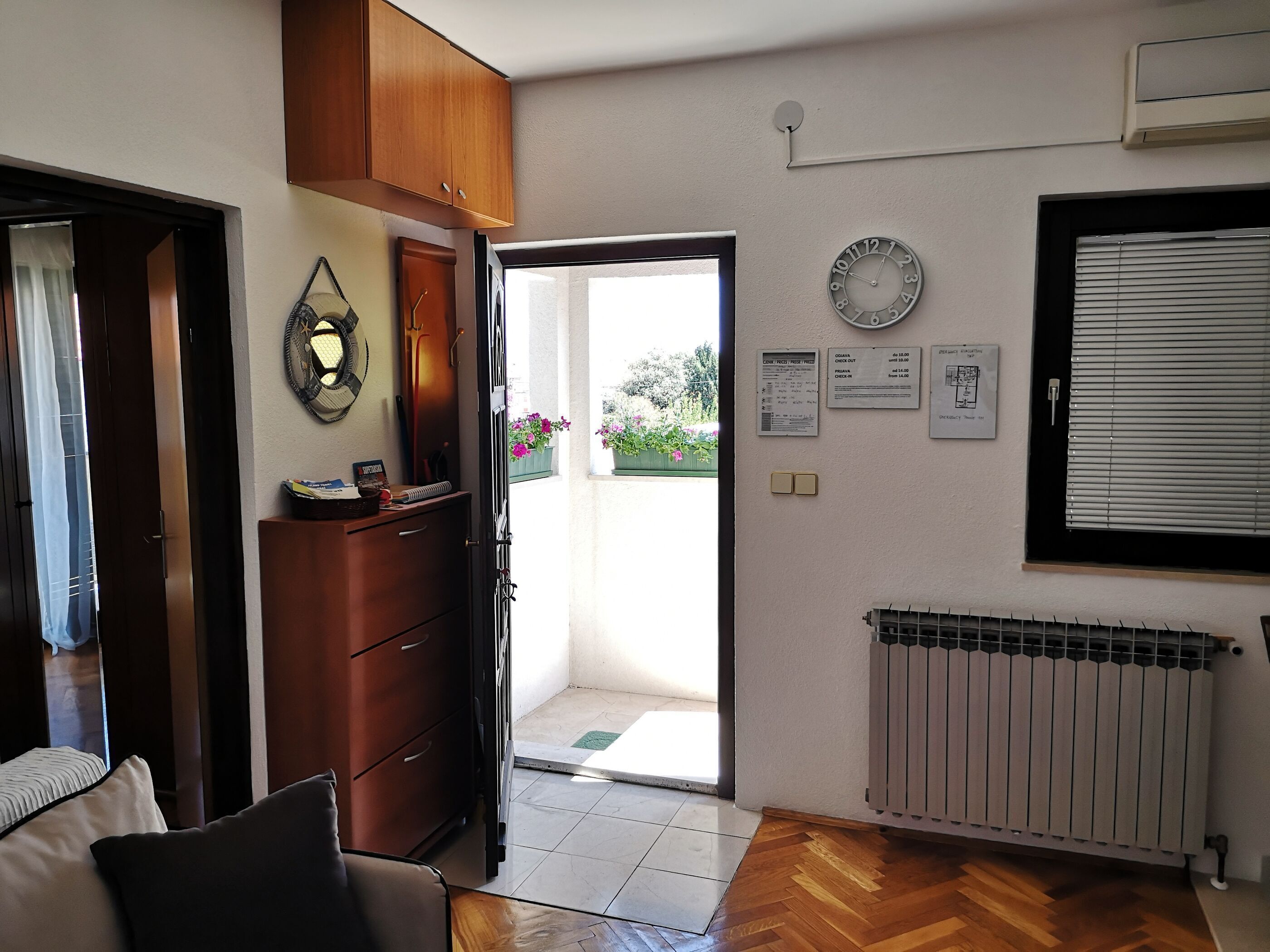 Una habitación con un armario de madera, un reloj, un radiador y una puerta que da a un espacio exterior con plantas.