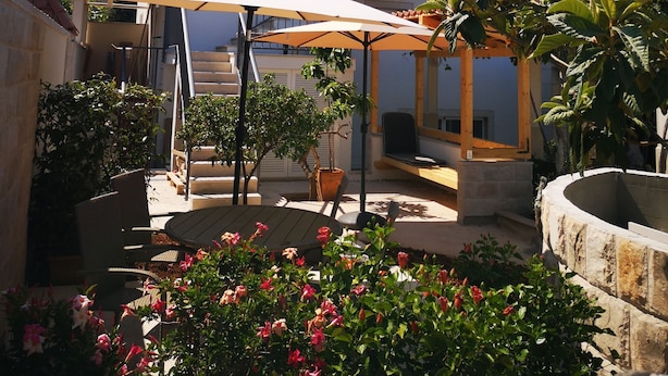 A two-story house with a balcony, a patio with a table and chairs, and a garden with flowers. - Apartments Natasa (Supetar)