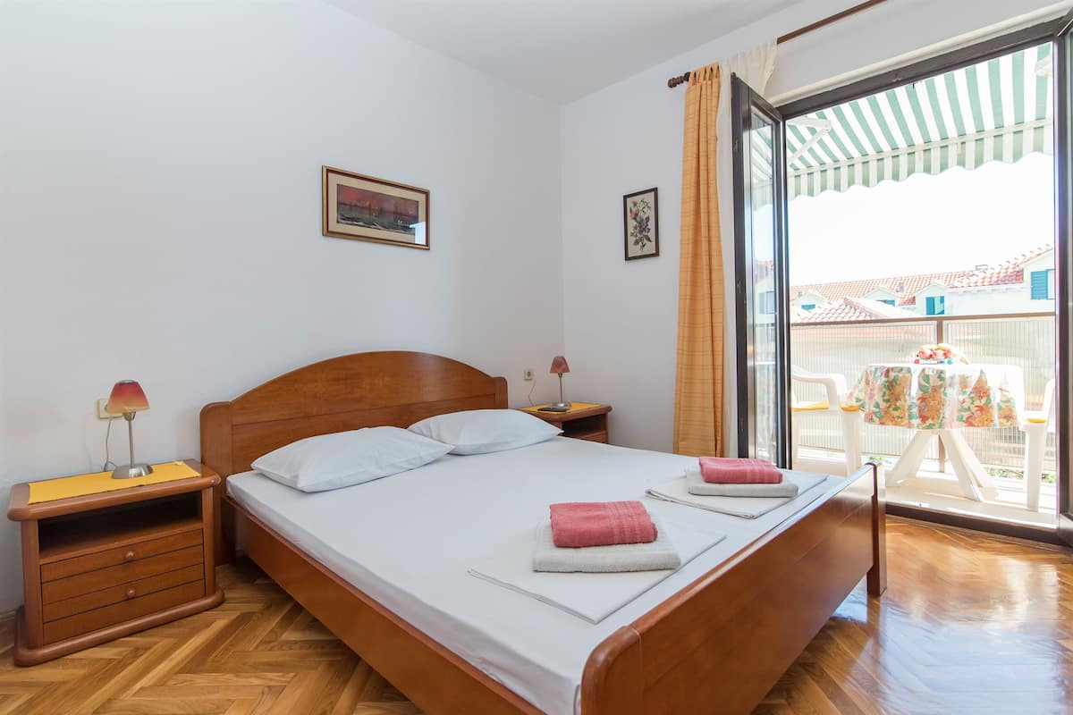 A bedroom with a wooden bed, two bedside tables, a nightstand, and a window with a view of the outside.