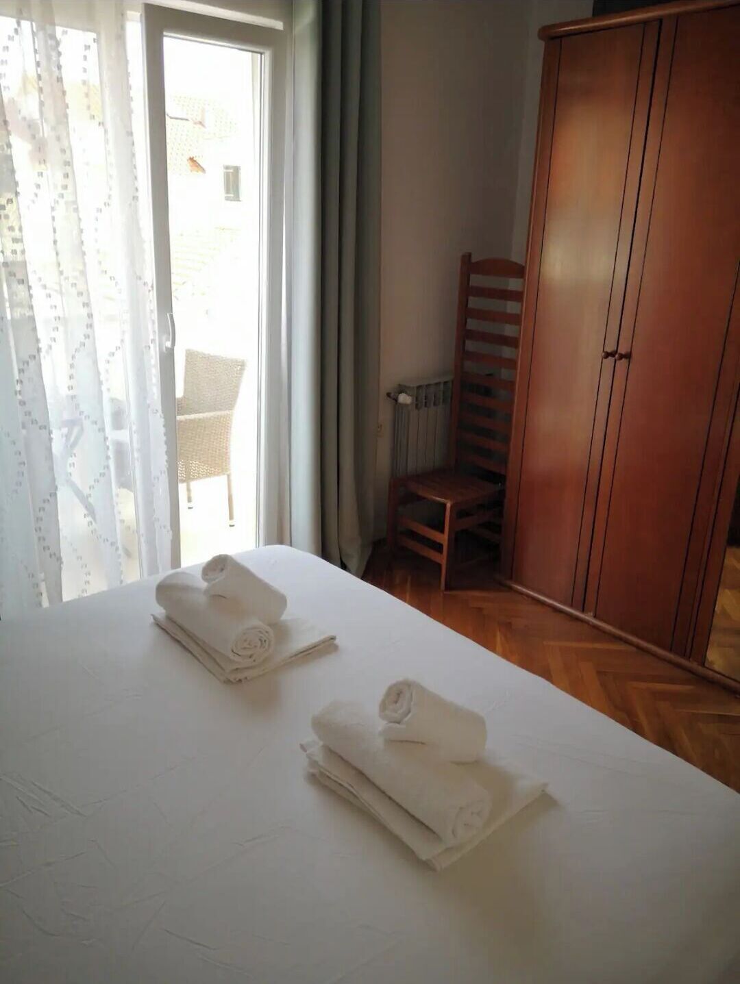 Hotelkamer met een bed, twee opgerolde handdoeken, een houten garderobe en een stoel.