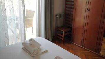 Hotelkamer met een bed, twee opgerolde handdoeken, een houten garderobe en een stoel.