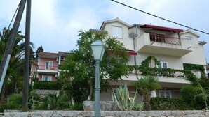 A multi-story residential building with a stone wall in the foreground, a street lamp, and lush greenery. - Apartment and Room Darinka (Vrboska)