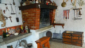A rustic kitchen with a brick fireplace, wooden bench, and various kitchen utensils.