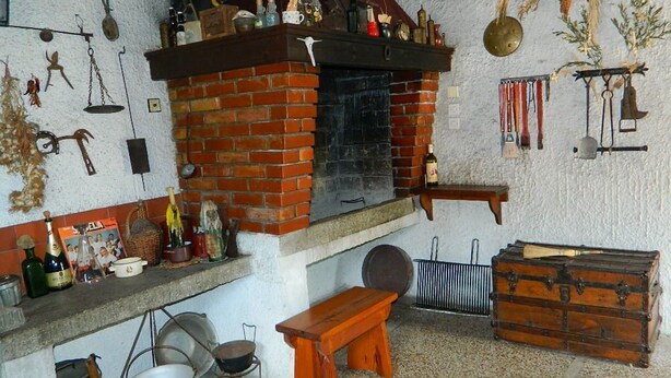 A rustic kitchen with a brick fireplace, wooden bench, and various kitchen utensils. - Apartment and Room Darinka (Vrboska)