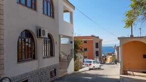 A narrow street with buildings, a car parked on the side, and a clear view of the sea in the background. - Apartments Verica (Makarska)