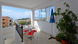 A balcony with a table and chairs, a potted plant, and a view of buildings and a body of water. - Apartments Verica (Makarska)