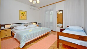 A bedroom with two beds, a wooden headboard, a bedside table with a lamp, a mirror, a framed picture on the wall, and a ceiling light fixture. - Apartments Verica (Makarska)