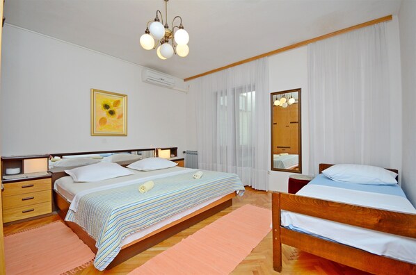 A bedroom with two beds, a wooden headboard, a bedside table with a lamp, a mirror, a framed picture on the wall, and a ceiling light fixture.