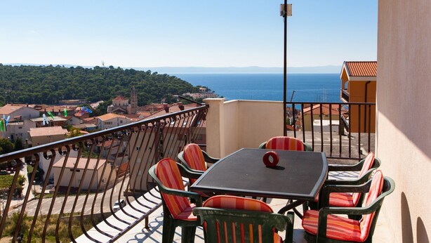 A balcony with a table and chairs, overlooking a coastal town and the sea. - Apartments Verica (Makarska)