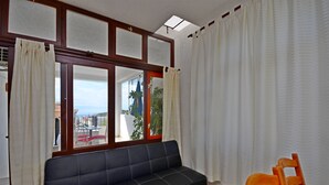 A room with a dark sofa, a wooden chair, a window with curtains, and a view of the outside. - Apartments Verica (Makarska)