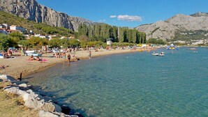 Una playa con agua cristalina, costa rocosa y montañas al fondo.