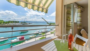 Un balcón con vistas a un puerto deportivo, una botella de vino y una mesa con copas.