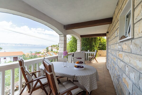 Un espace de restauration extérieur abrité, avec une table dressée pour deux personnes, un mur en pierre et une vue sur la mer.
