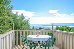 A balcony with a round table and chairs, overlooking a scenic view of the sea and mountains.