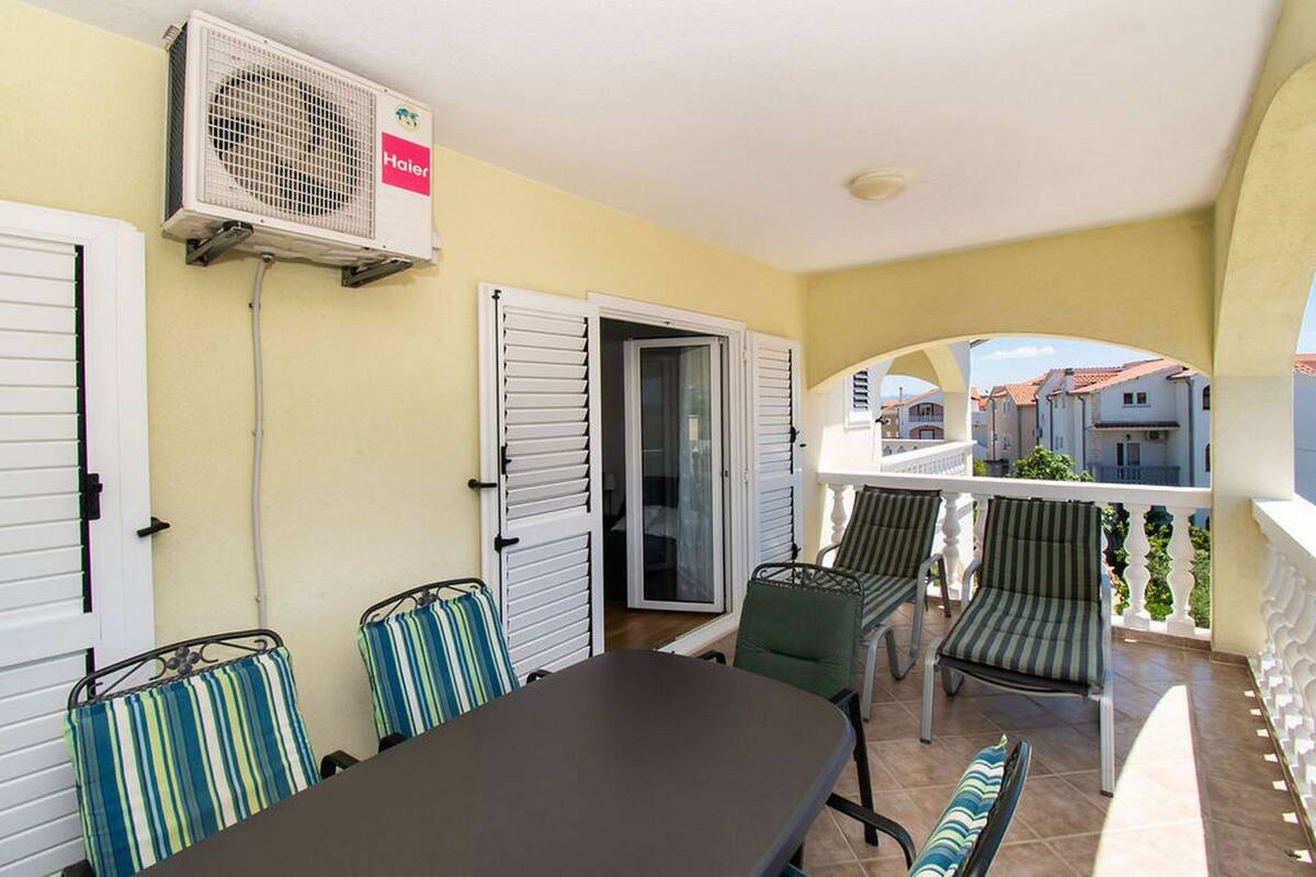 A balcony with a table and chairs, an air conditioning unit, and a view of the surrounding buildings.