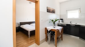 Quarto compacto com cama, pequena mesa de jantar com cadeiras, cozinha equipada com pia e armários, e uma janela.
