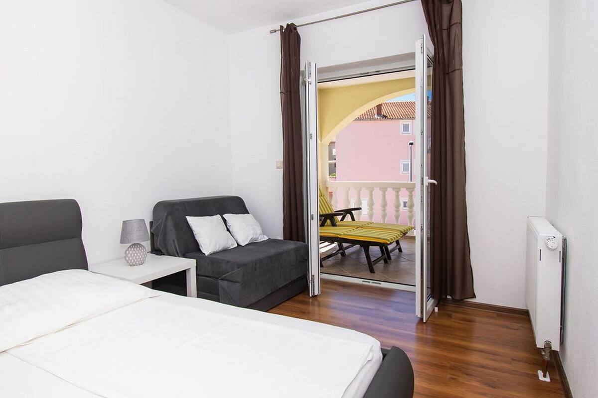 A hotel room with a bed, a sofa, a small table with a lamp, and a balcony with a chair and a table.
