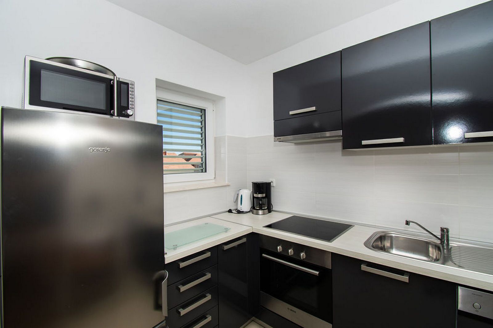 A compact kitchen with a refrigerator, microwave, stove, sink, and black cabinets.