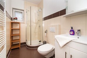 Un baño moderno con cabina de ducha de vidrio, inodoro, lavamanos con toalla y estante de madera con flores.