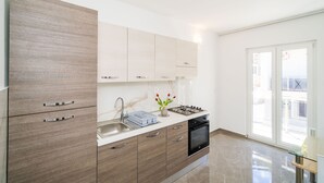 A modern kitchen with a built-in stove, a sink, and a dishwasher. There is a window providing natural light and a view of the outside. - Apartment and Rooms Mato (Mlini)