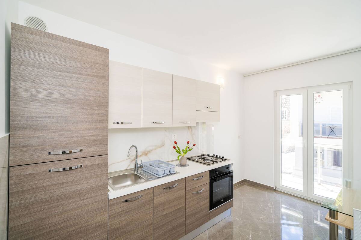 A modern kitchen with a built-in stove, a sink, and a dishwasher. There is a window providing natural light and a view of the outside.