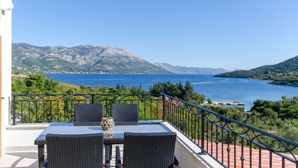 A balcony with wicker furniture and a view of a coastal landscape. - Apartments Koras (Kneza)