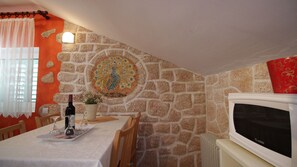 Comedor con pared de piedra, un mosaico decorativo, una mesa dispuesta con botella de vino, copas y un florero.