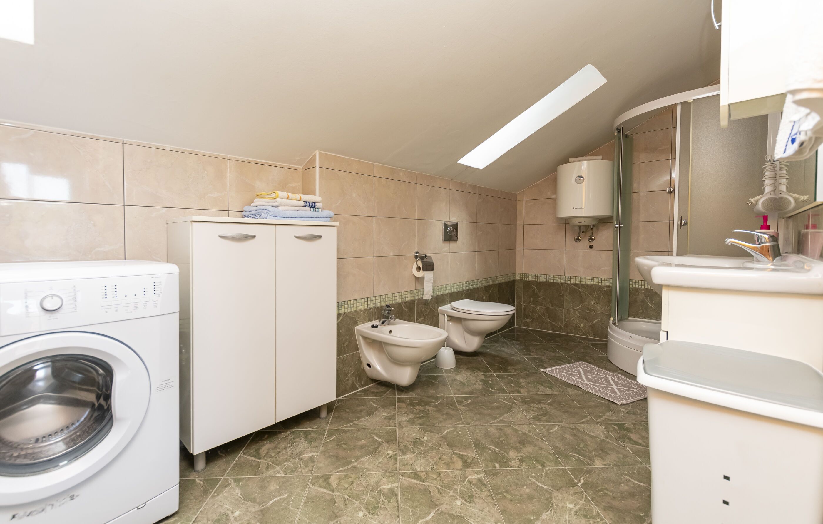 Un baño moderno con lavadora, dos inodoros, un lavamanos y zona de ducha.
