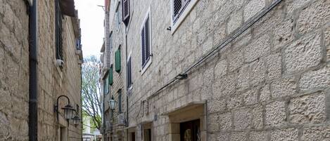 A narrow stone-paved alleyway flanked by buildings with traditional architecture, including visible doors and windows.