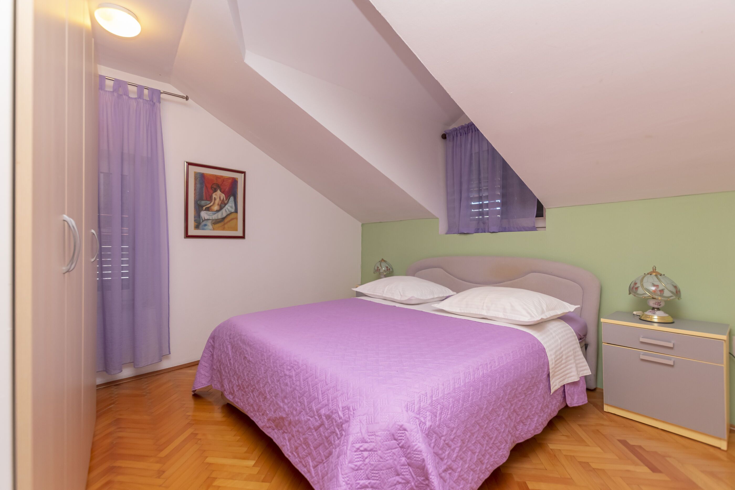 A bedroom with a bed, a nightstand, a lamp, and a painting on the wall.