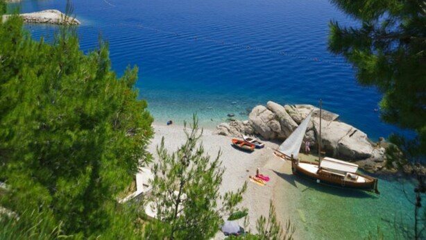 Ein Strand mit klarem türkisblauem Wasser, einer felsigen Küstenlinie und einem Segelboot, das in der Nähe vor Anker liegt.
