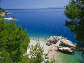 A beach with clear turquoise water, a rocky shoreline, and a sailboat anchored near the shore. - Rooms Jakirusa (Brela)