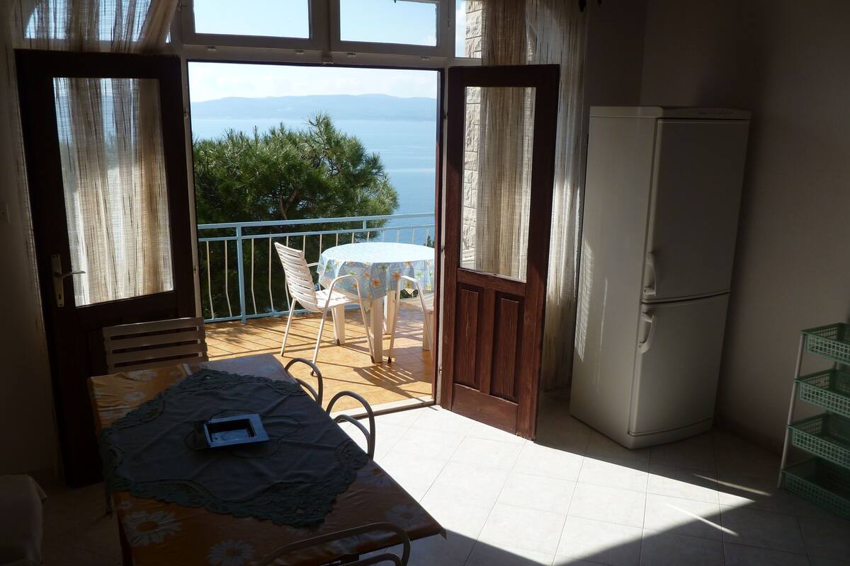 Un balcon avec une table et des chaises, un réfrigérateur et une vue sur la mer.
