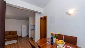 A dining area with a wooden table set for four, a bottle of wine, and a bowl of fruit. - Apartments Oliver (Putnikovic)