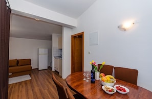 Comedor con una mesa de madera dispuesta para cuatro, una botella de vino y un cuenco de fruta.